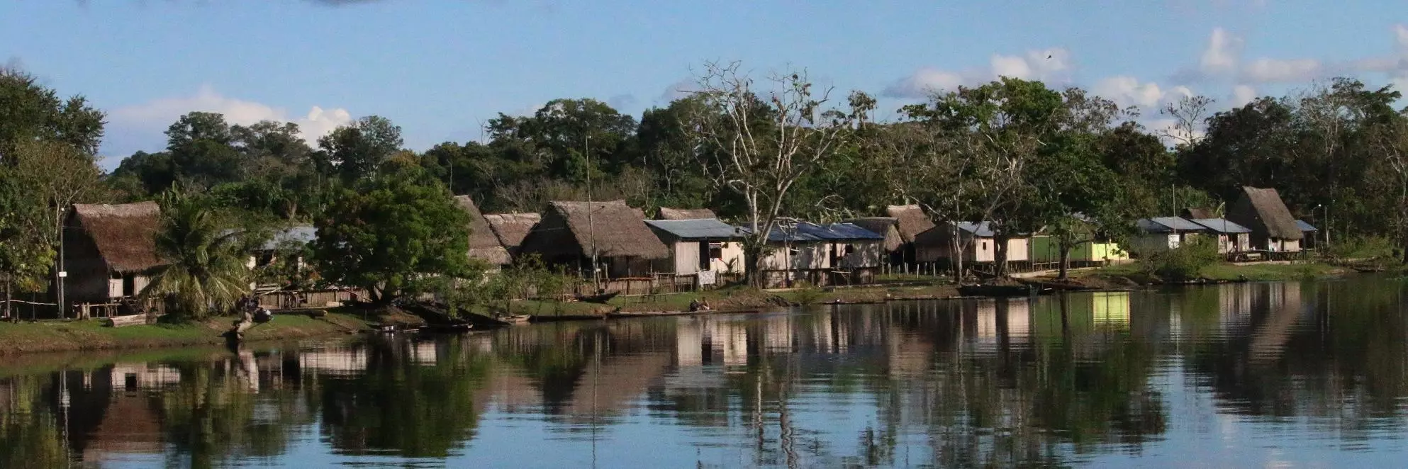Sarah Papworth's peruvian amazon photo,  river and houses along the bank. reflection of blue sky and clouds in the river